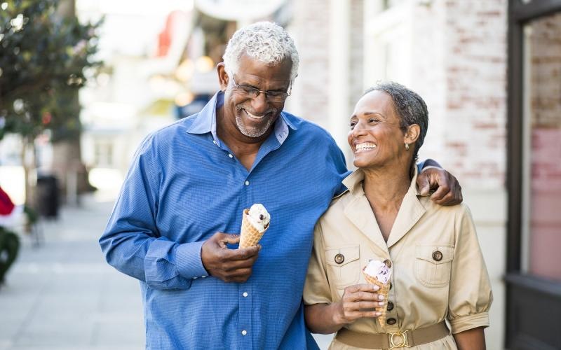older couple walks down city sidewalk while holding ice cream cones