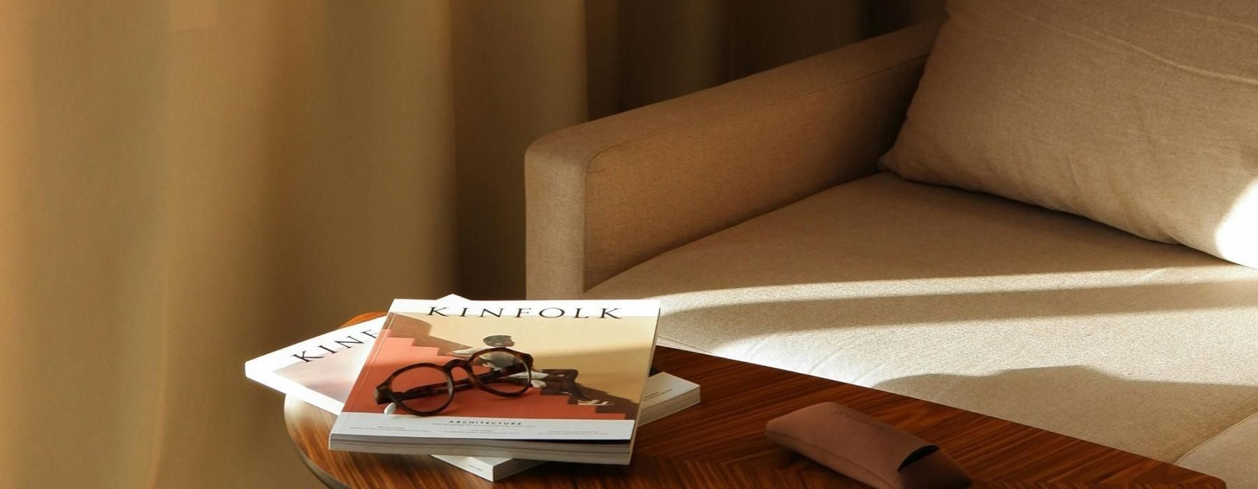 A table with a book and glasses on it next to a couch in the sunlight.