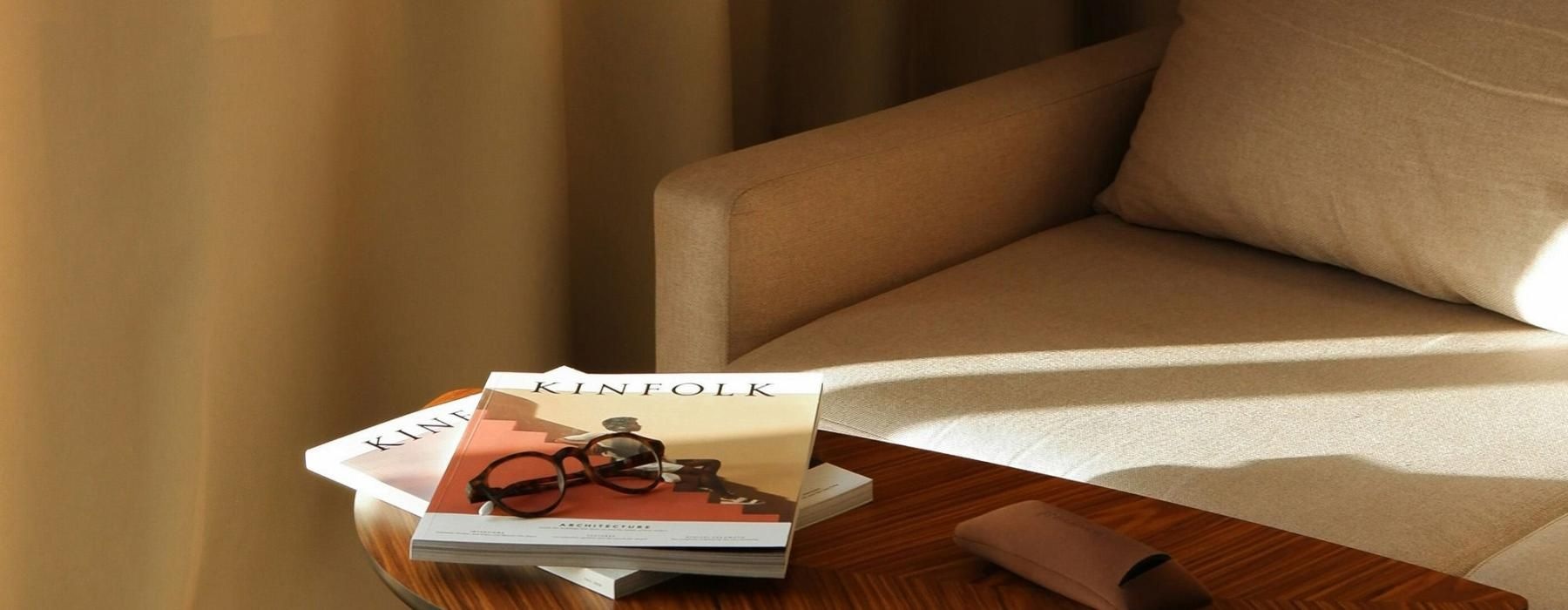 A table with a book and glasses on it next to a couch in the sunlight.